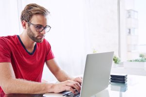 Man in red shirt typing on a laptop.