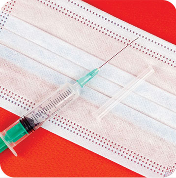 Syringe and needle sitting on a white facial mask.