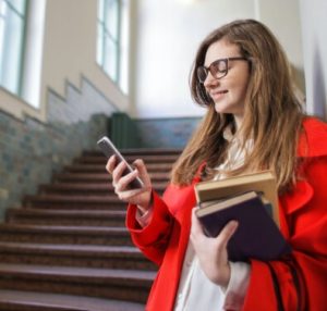 Woman looking at phone while holding books