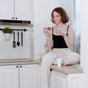 Woman paying bills on phone, in her kitchen at home