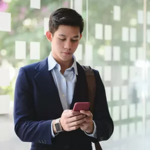 young man in suit coat looking at this texts in a busy office