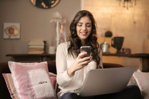 woman looking at cell phone while on laptop